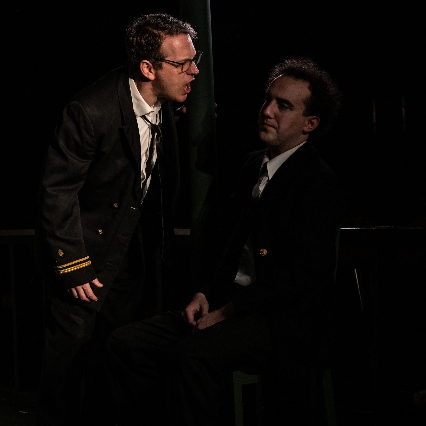 Two men in suits and ties are standing next to each other in a dark room.