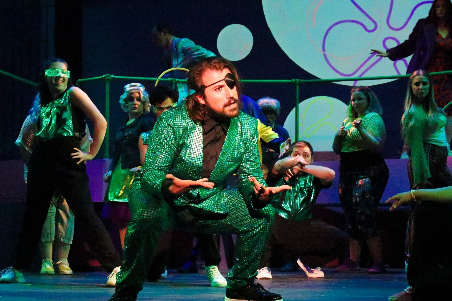 A man in a green suit is kneeling down on a stage in front of a group of people.