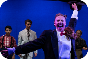 A man in a tuxedo and bow tie holds his hat in the air