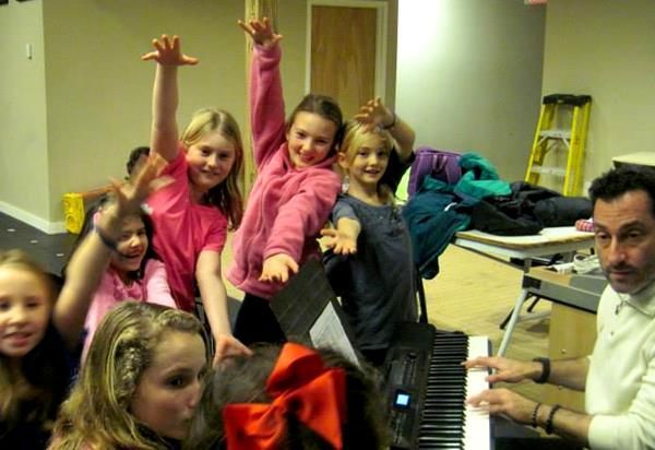 A group of children are posing for a picture while a man plays the piano