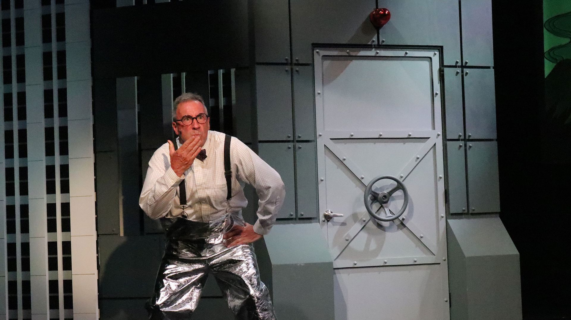 A man is standing on a stage in front of a vault door.