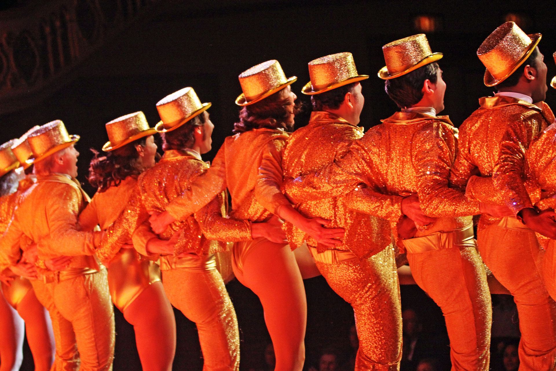 A group of people wearing gold outfits and top hats