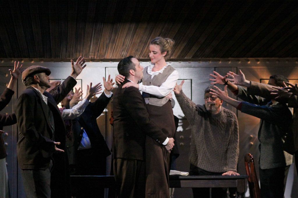 A group of people are standing around a man and a woman on a stage.