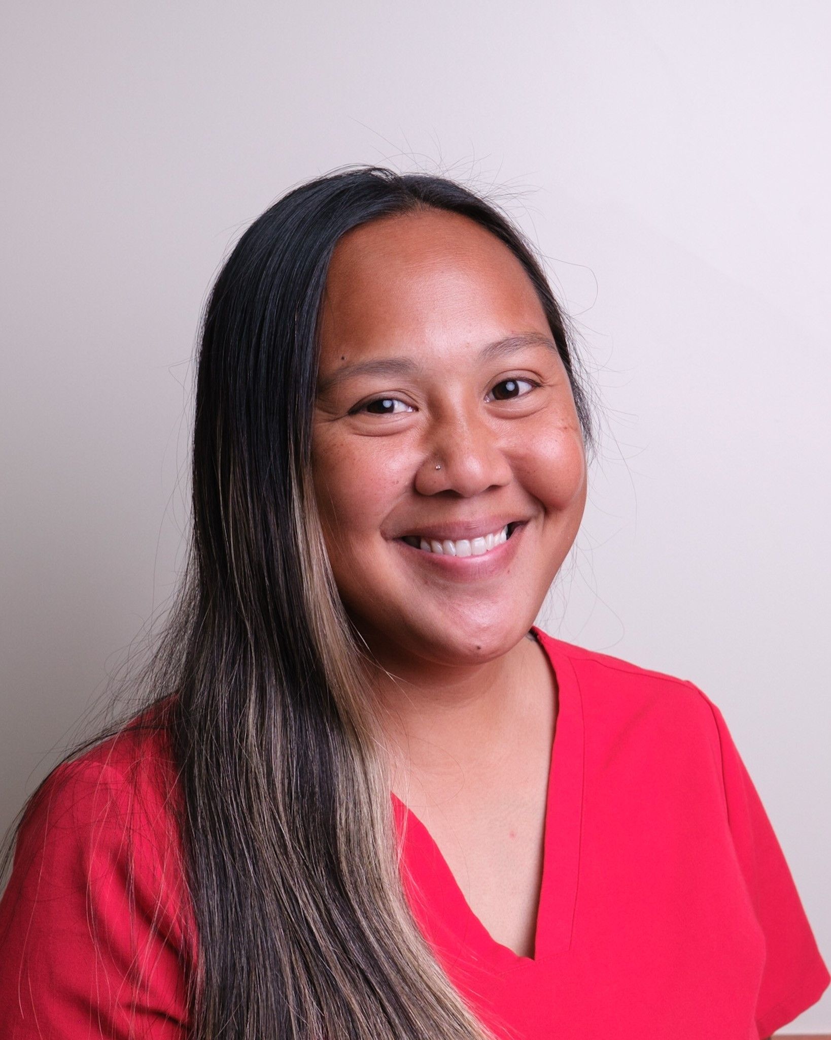Woman with long dark and light hair smiles in a red shirt.