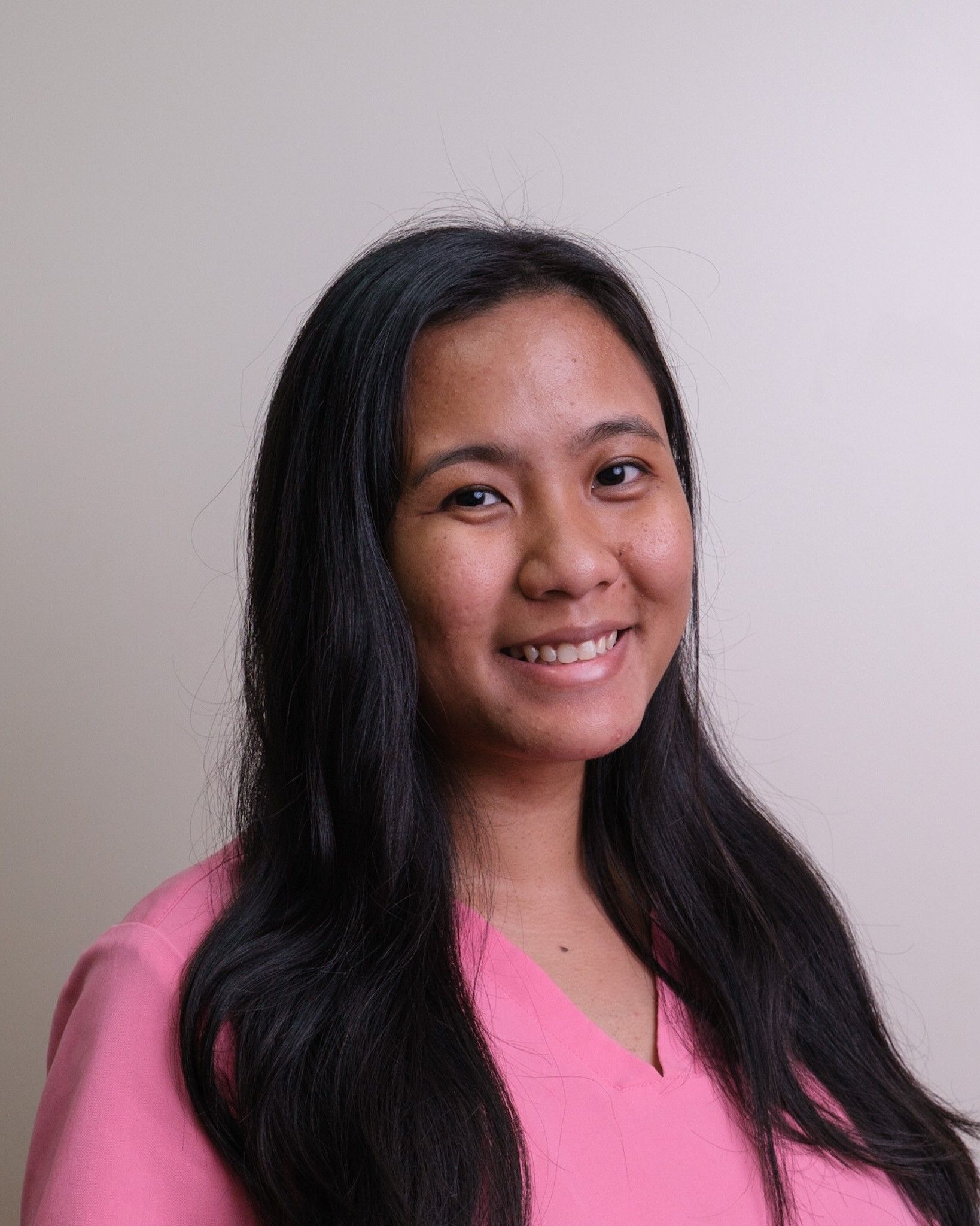 Woman with long black hair and a pink top, smiling.
