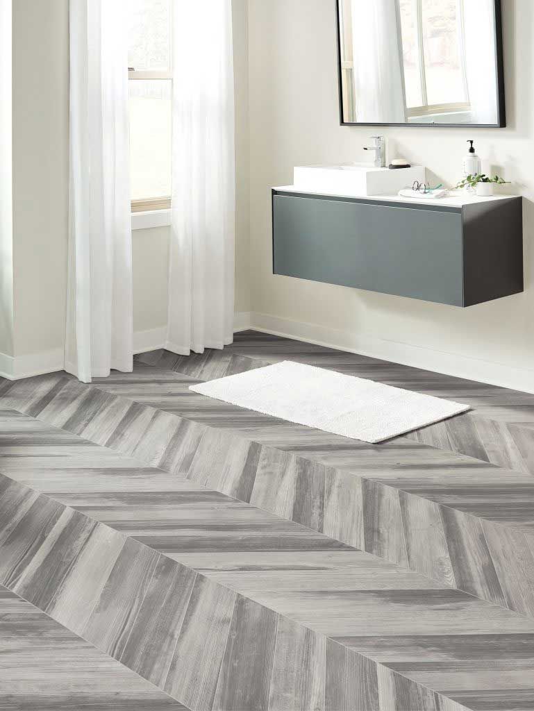 Bathroom with gray herringbone floor, floating vanity, and white rug.