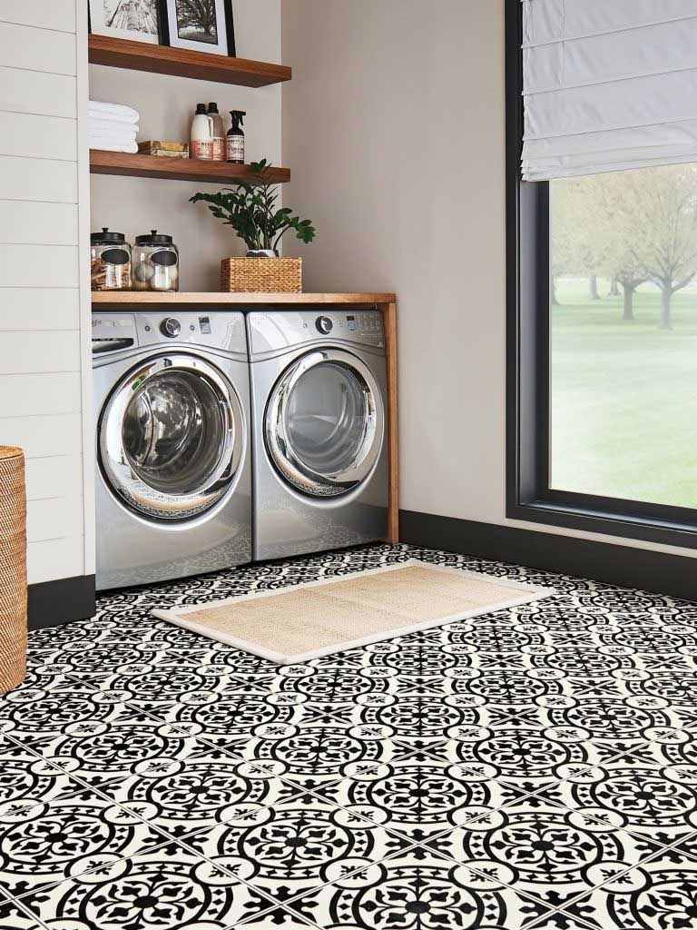Laundry room with black and white patterned floor, washer and dryer, and shelves with décor.