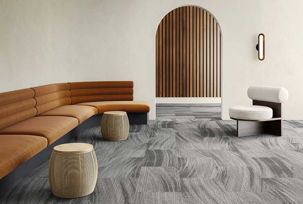A modern lounge area with a brown sectional, patterned gray carpet, wooden stools, and arched wood paneling.
