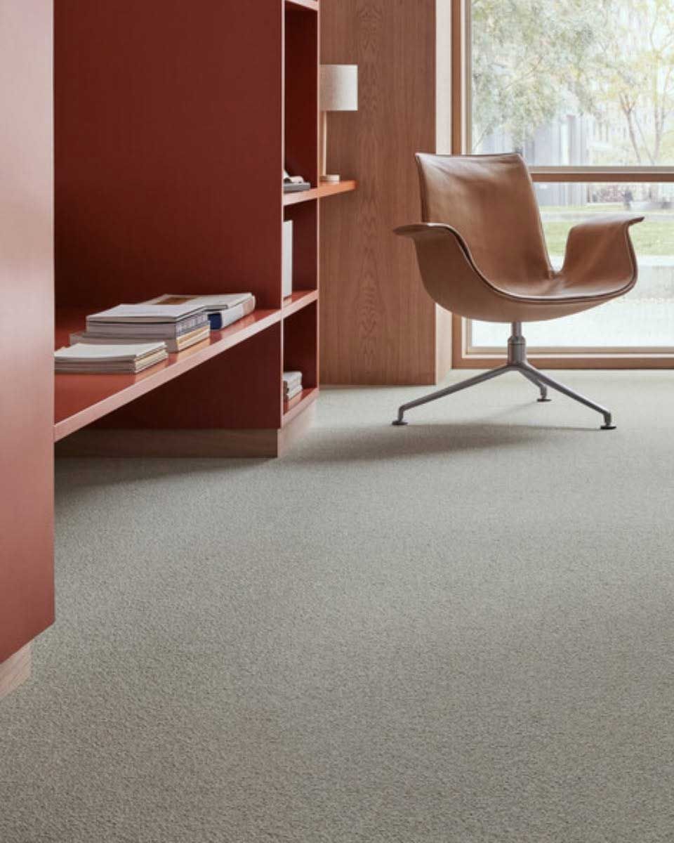 Modern room with gray carpet, built-in red shelving, brown leather chair, and window with natural light.