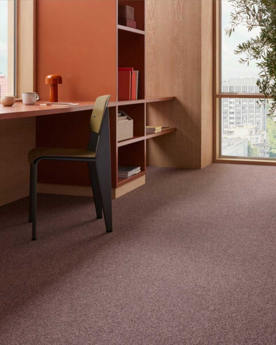 Desk with chair, built-in shelves, and window, all in warm tones, on a purple carpet.