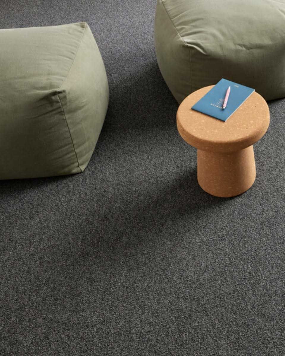 Gray speckled carpet with green beanbag chairs and a cork side table holding a notepad and pen.