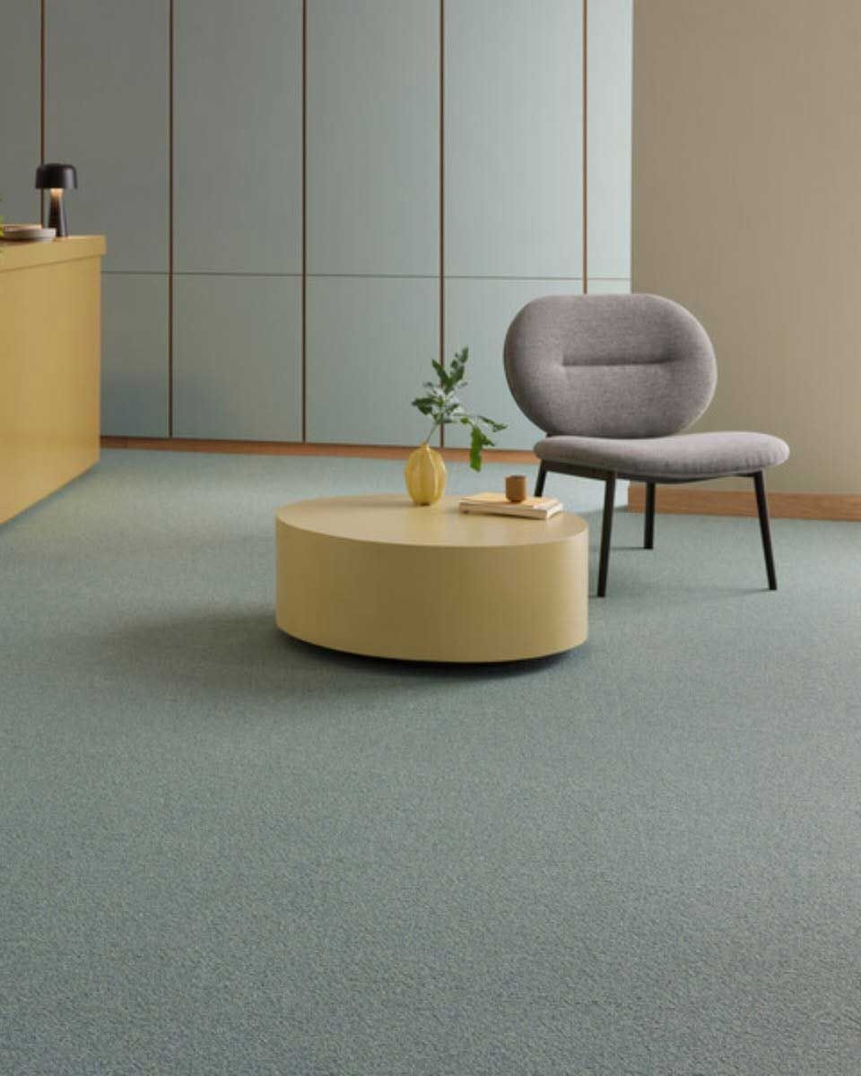 Room interior with blue-green carpet, round yellow coffee table, gray chair, and light blue panel wall.