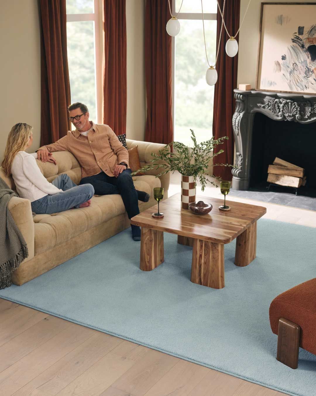 Couple relaxing on a beige sofa in a living room with a blue rug and wooden coffee table.