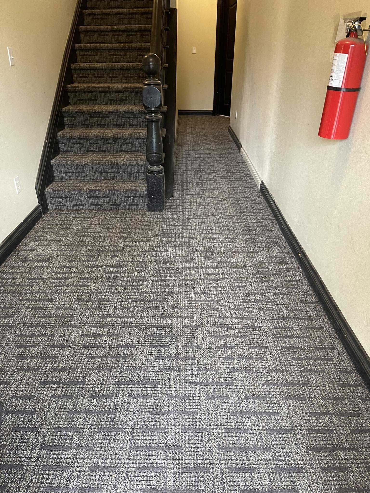 Narrow hallway with stairs and patterned carpet. A fire extinguisher hangs on the wall.