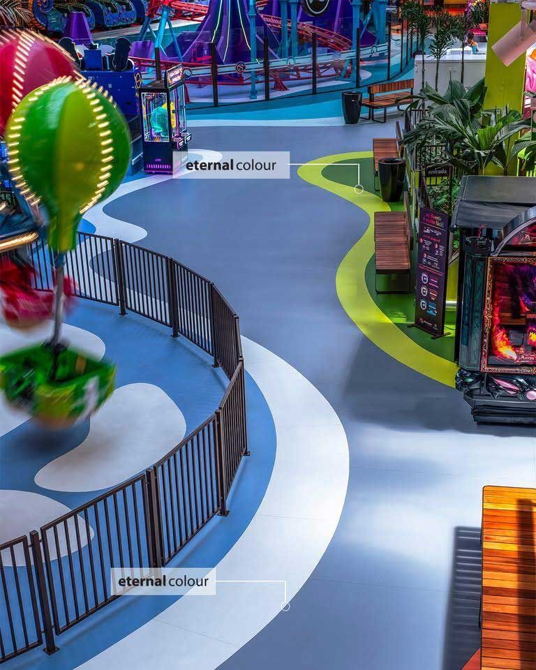 Indoor amusement park with winding blue and green paths, fences, and colorful rides.