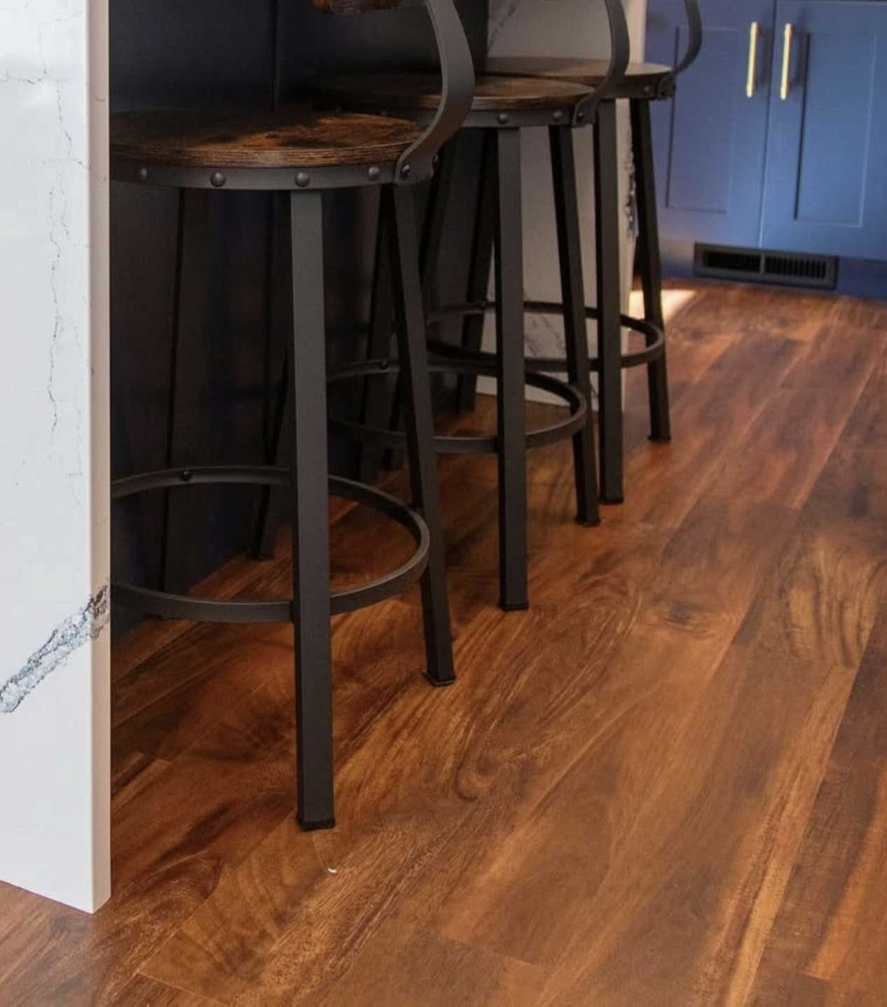 Three black bar stools with wooden seats on a hardwood floor, next to a kitchen counter.