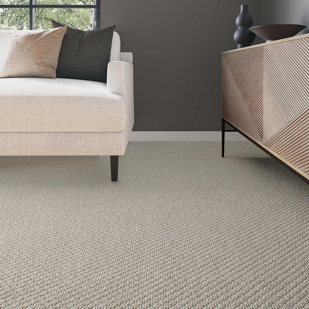 Living room with neutral carpet, sofa, and sideboard. Window in background, gray wall.