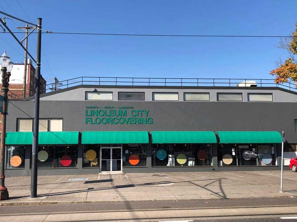 Lincoln City Floorcovering store exterior with green awning, large colorful circles, and teal lettering on gray building.