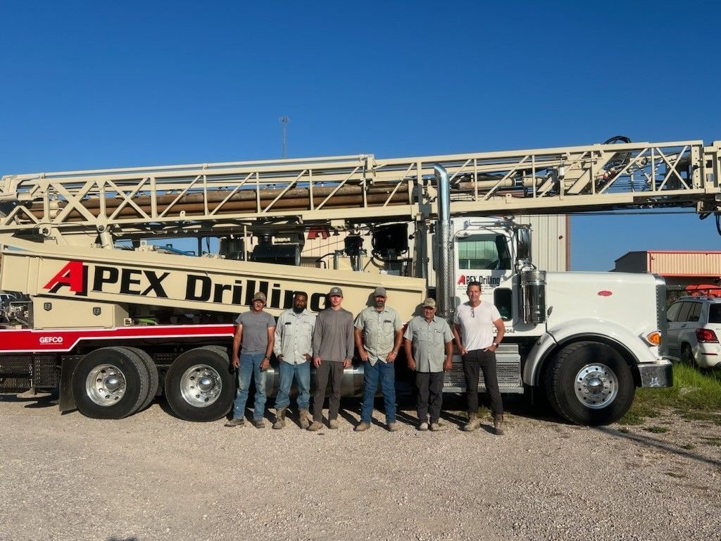 A group of men standing in front of an apex drilling truck