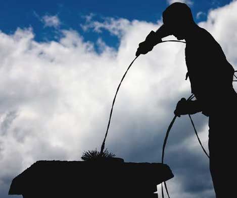 Silhouette of a chimney sweep cleaning a chimney against a cloudy sky.