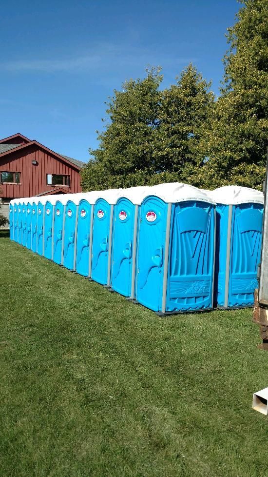 A row of blue portable toilets are lined up in a grassy field.
