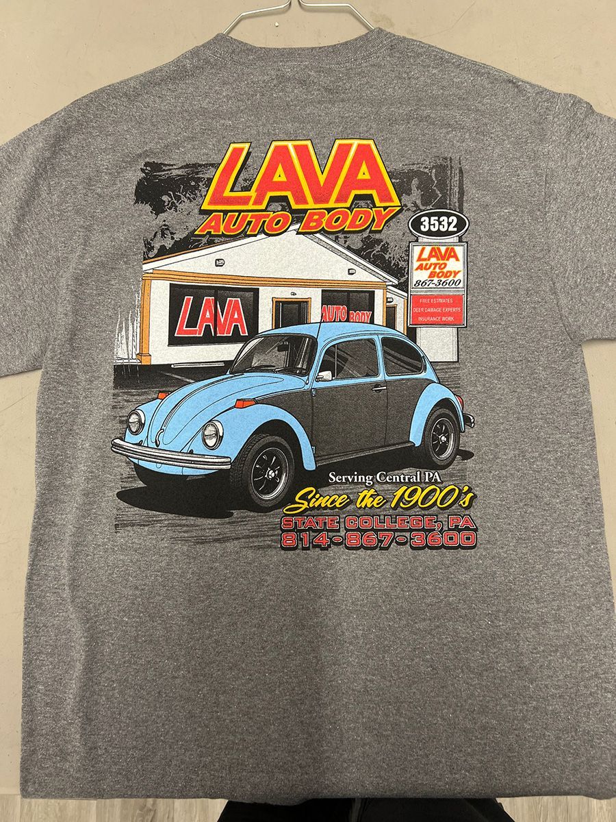 A grey t-shirt featuring a graphic of a light blue Volkswagen Beetle parked in front of a building labeled Lava Auto Body.