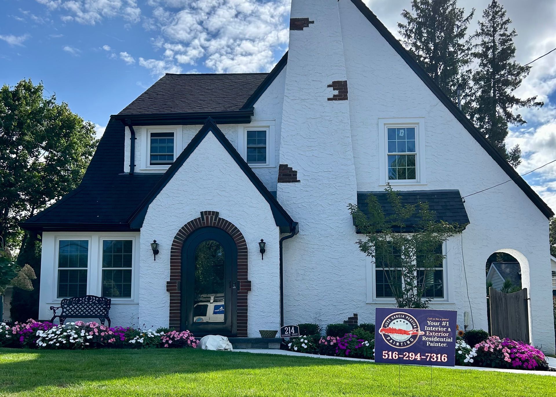 A white house with a black roof and a sign in front of it
