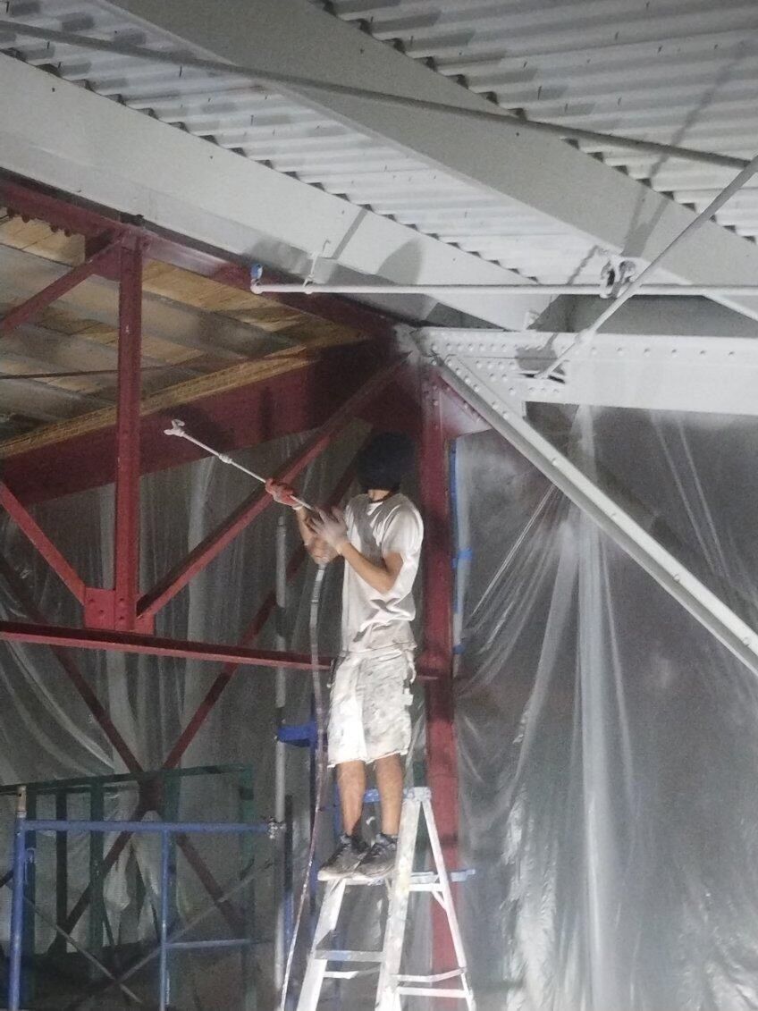 A man is standing on a ladder painting a ceiling