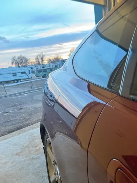 Red car's side, window, and wheel in a garage with a sky background; trailers are visible.