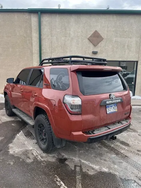 Red Toyota 4Runner SUV with black roof rack and wheels parked on a wet, snowy surface.