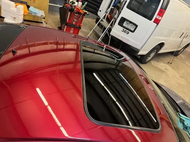 Red car roof with black sunroof, reflection of a garage, and a white van.