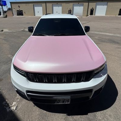 White SUV with a pink hood parked in front of a building with garage doors.