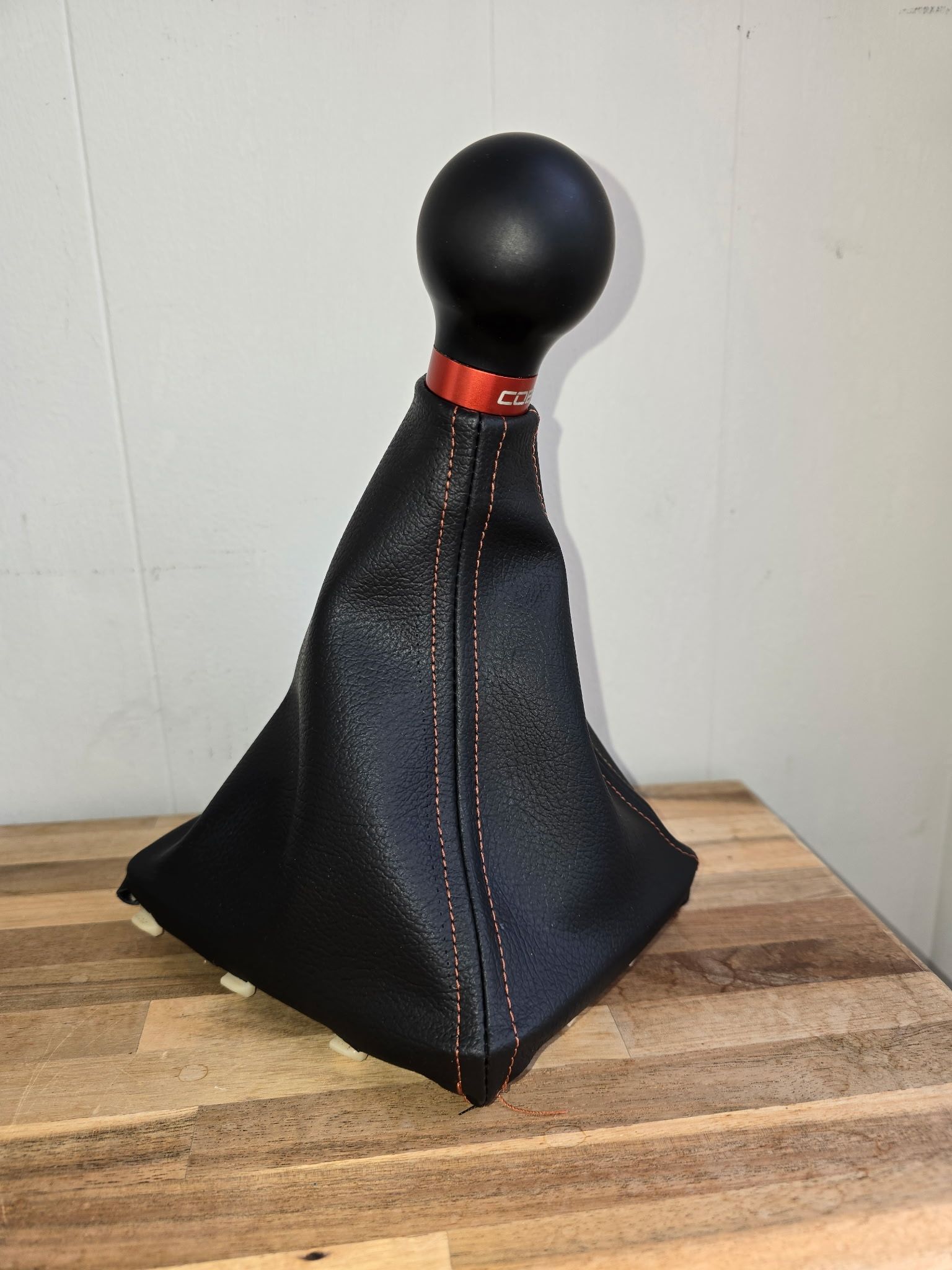a black leather gear shifter cover with a red stitching is sitting on a wooden table