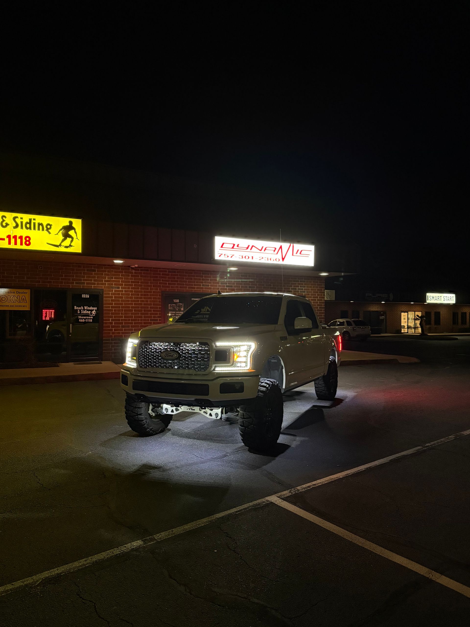 A white truck is parked in a parking lot at night