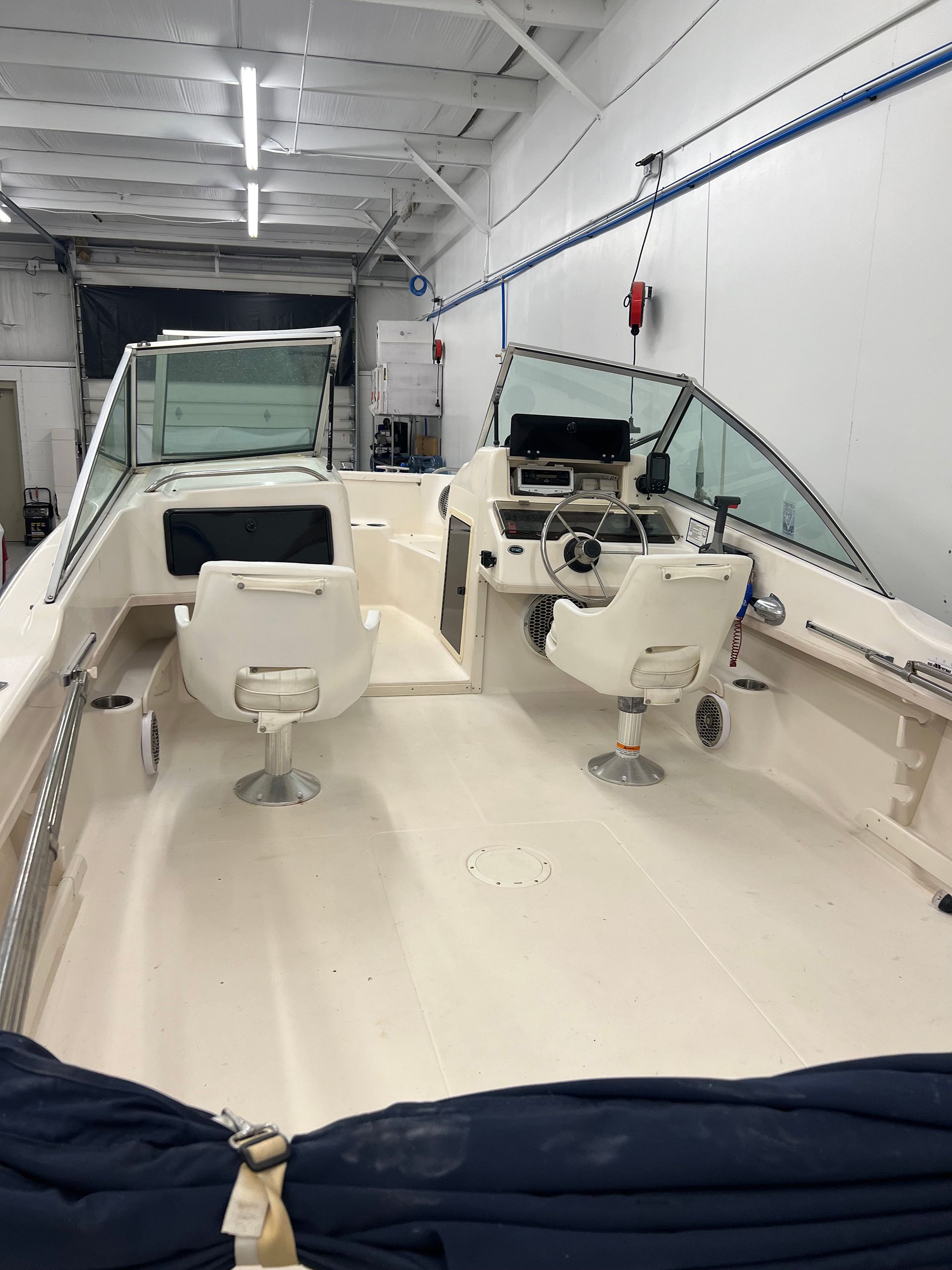 A boat is sitting in a garage with two chairs on the deck.