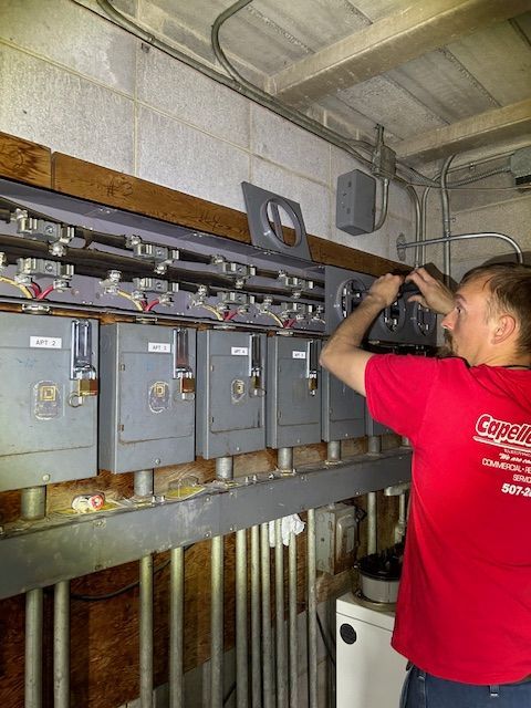 Electrician in red shirt working on electrical panel in a gray, concrete room.