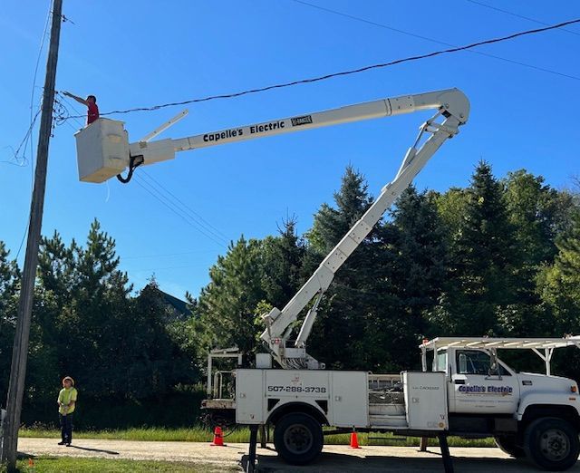 Lineman in bucket truck repairing power lines on sunny day. Another worker watches below.