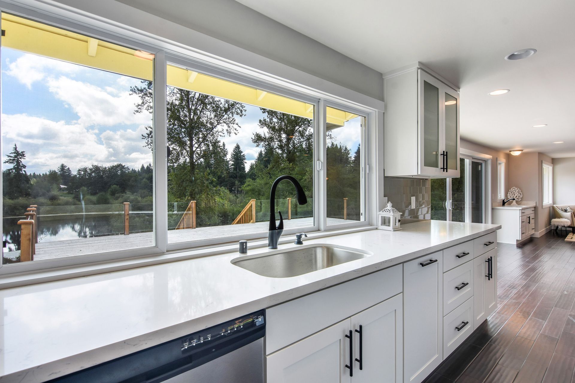 A kitchen with white cabinets , a sink , and a view of a lake.
