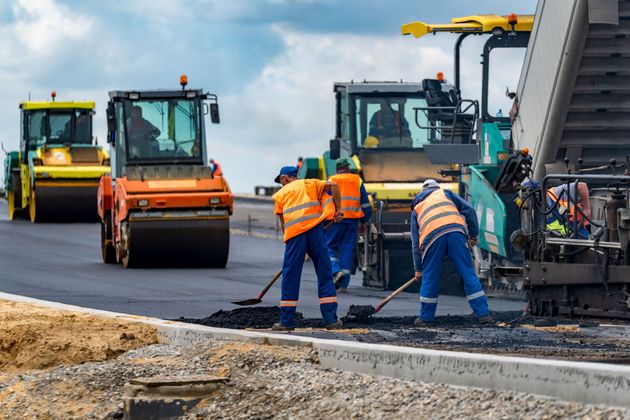 Road workers in orange vests paving a road beside heavy construction vehicles