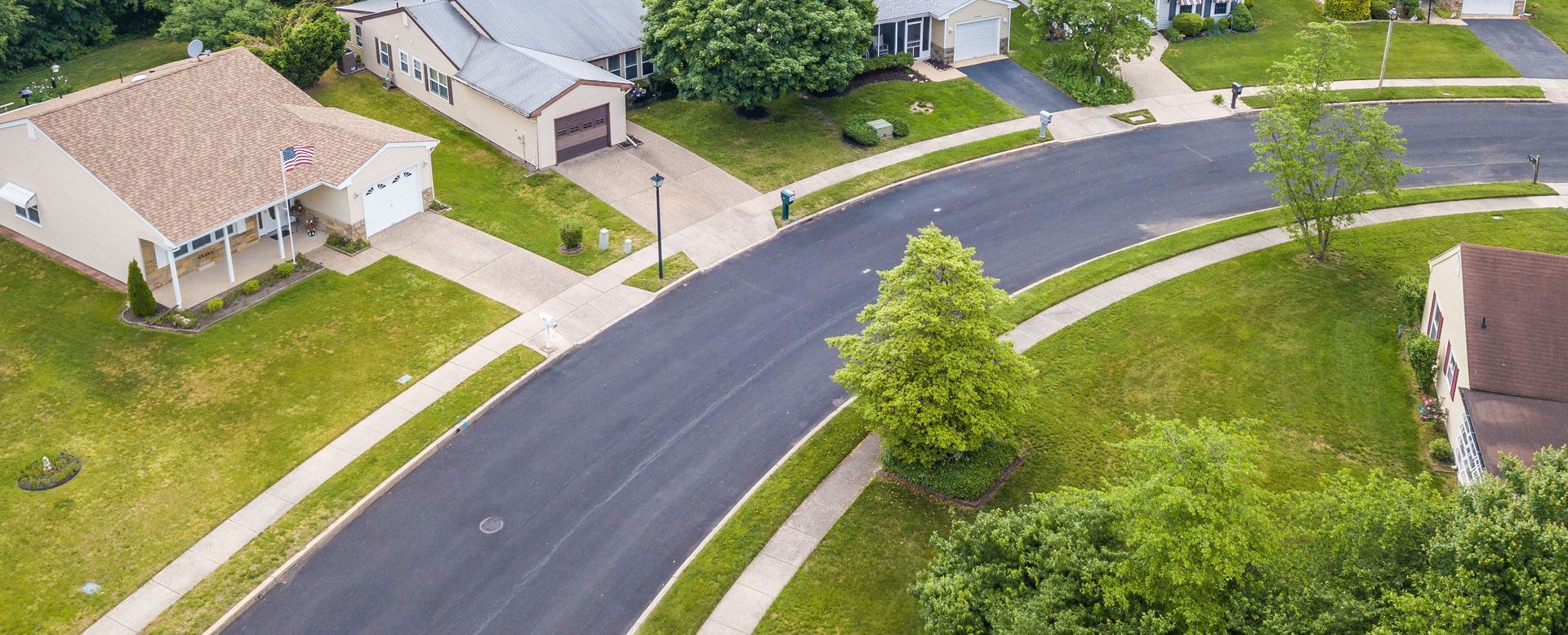 Aerial view of a quiet suburban neighborhood with curved roads, houses, lawns, and trees.