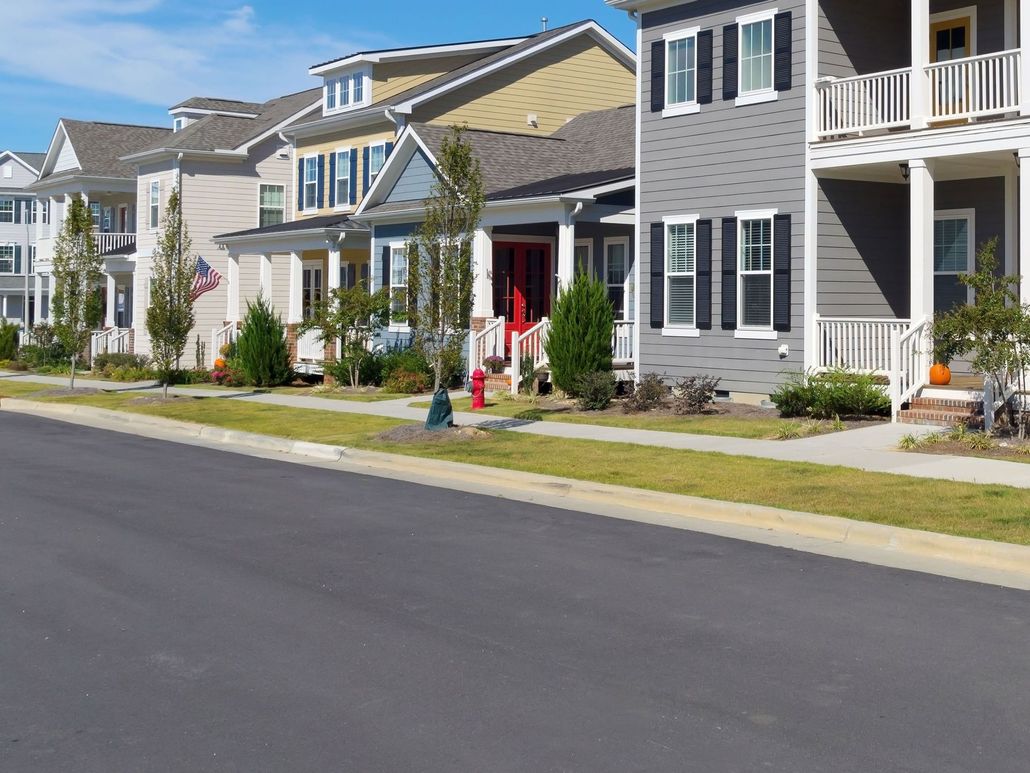 Suburban row of townhouses with front porches, green lawns, and a quiet paved street in the foreground