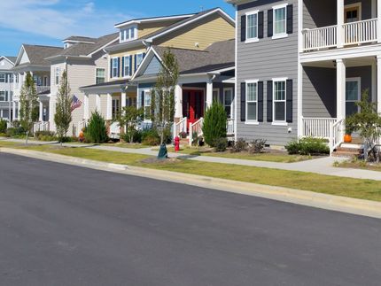 Suburban row of townhouses with front porches, green lawns, and a quiet paved street in the foreground