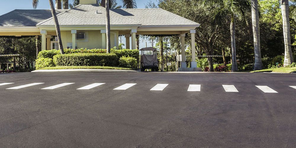 Driveway entrance with a white house, palm trees, and a road with crosswalk markings
