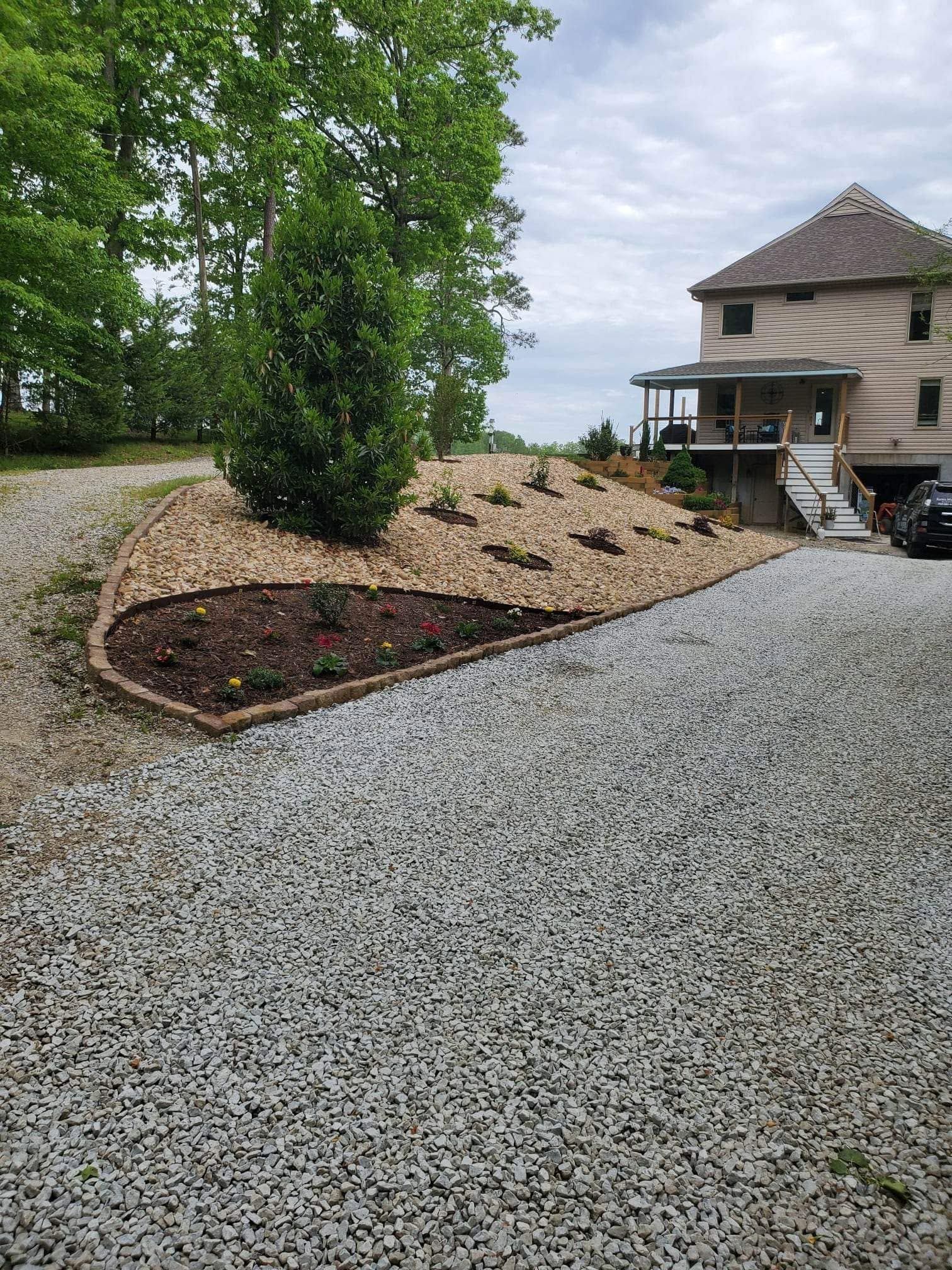 Gravel driveway beside a landscaped yard with a house and deck in the background.