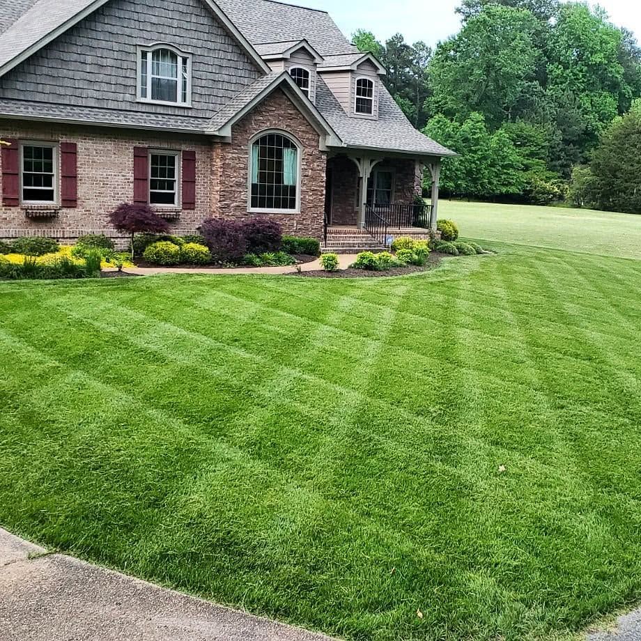 Brick house with gray roof and neatly striped green lawn in a suburban yard