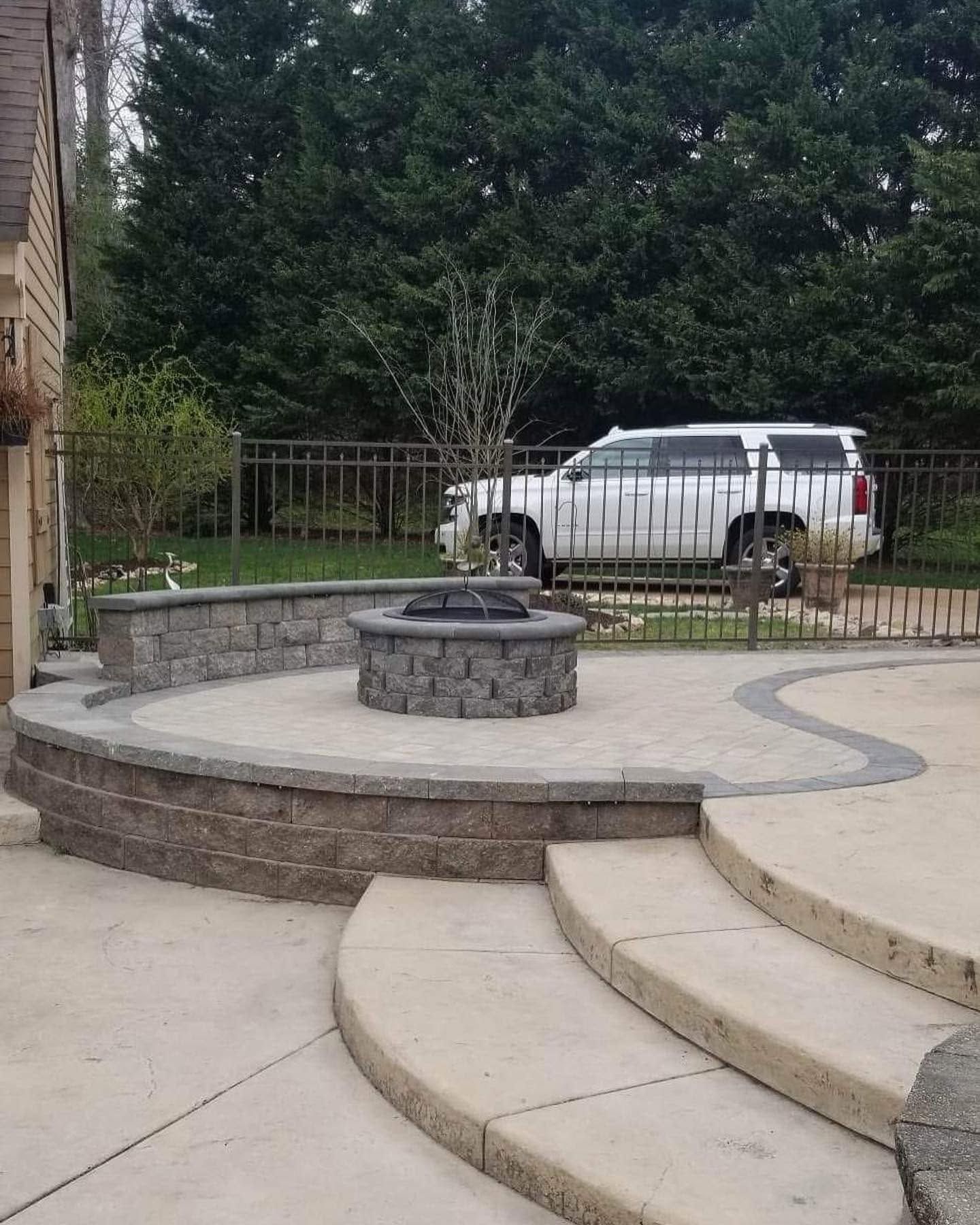 Stone steps and a circular fire pit in a courtyard, with a white SUV parked behind a fence.