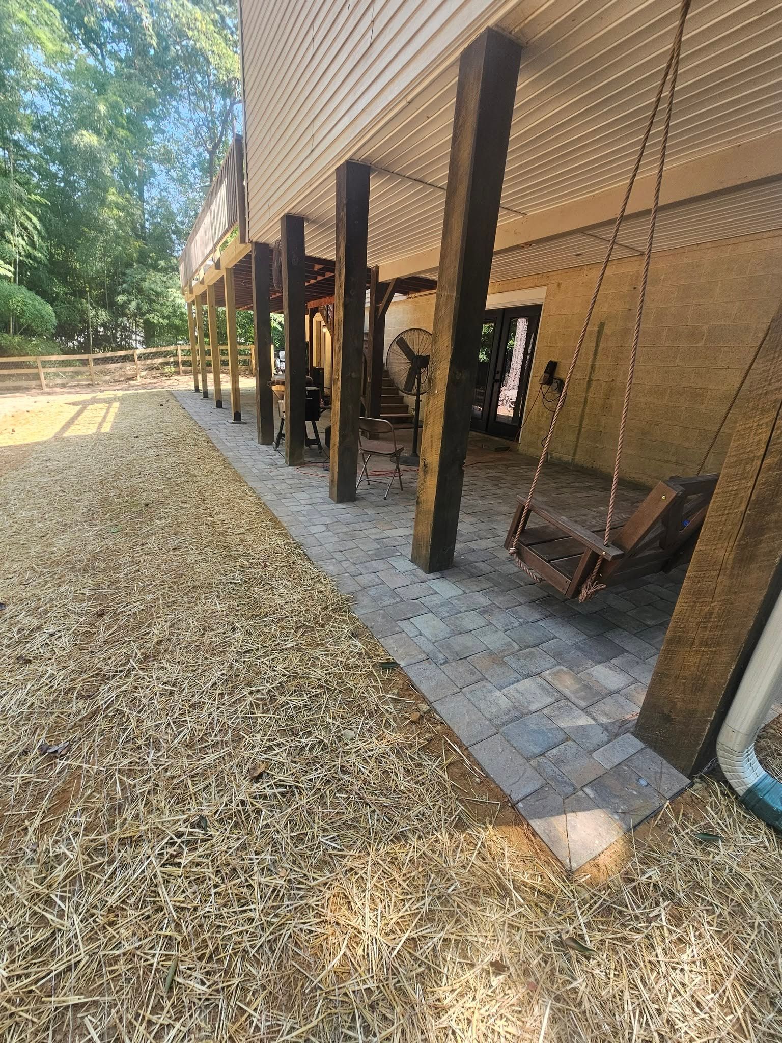 Wooden deck and shaded patio beneath a raised building, with gravel path and outdoor furniture.