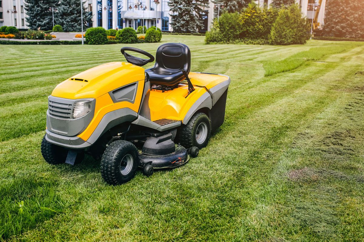 Yellow riding lawn mower on a grassy lawn near a building.