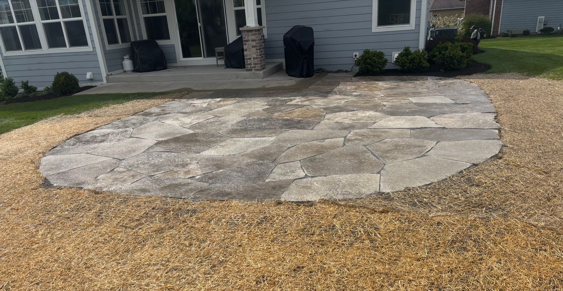 Stone patio in a backyard with a house and gravel ground nearby.