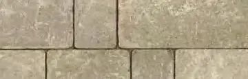 A close-up view of beige, rectangular stone pavers arranged in a repeating pattern with thin, dark grout lines.